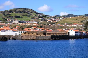 A coastal town with a historic stone wall, red-roofed buildings, and a hill in the background. - Monte da Guia Alojamento Local (Horta)