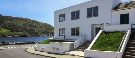 A modern white building with a staircase leading to the entrance, situated by a body of water.