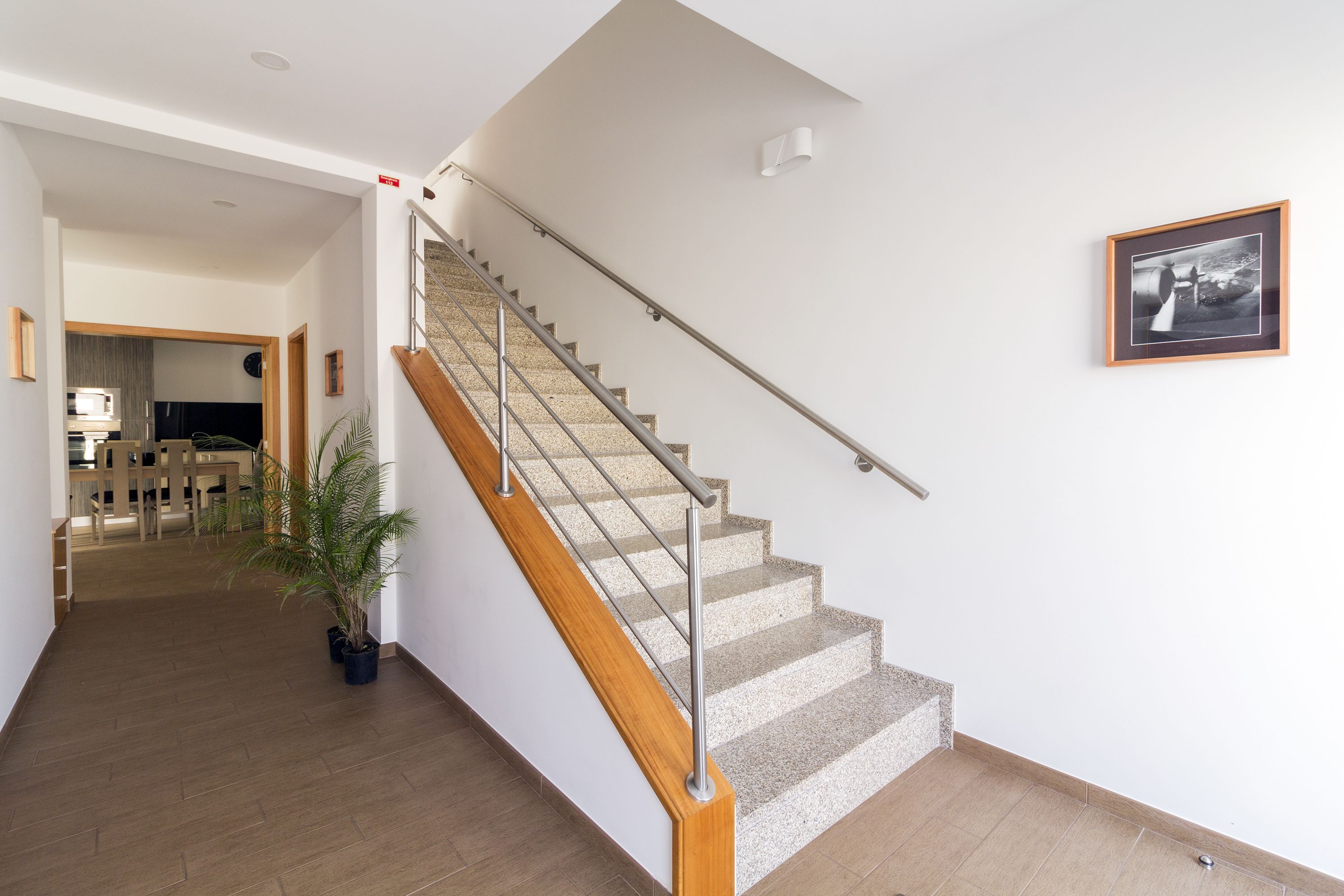 Una escalera con barandilla de madera y balaustrada metálica, que conduce a un piso superior.