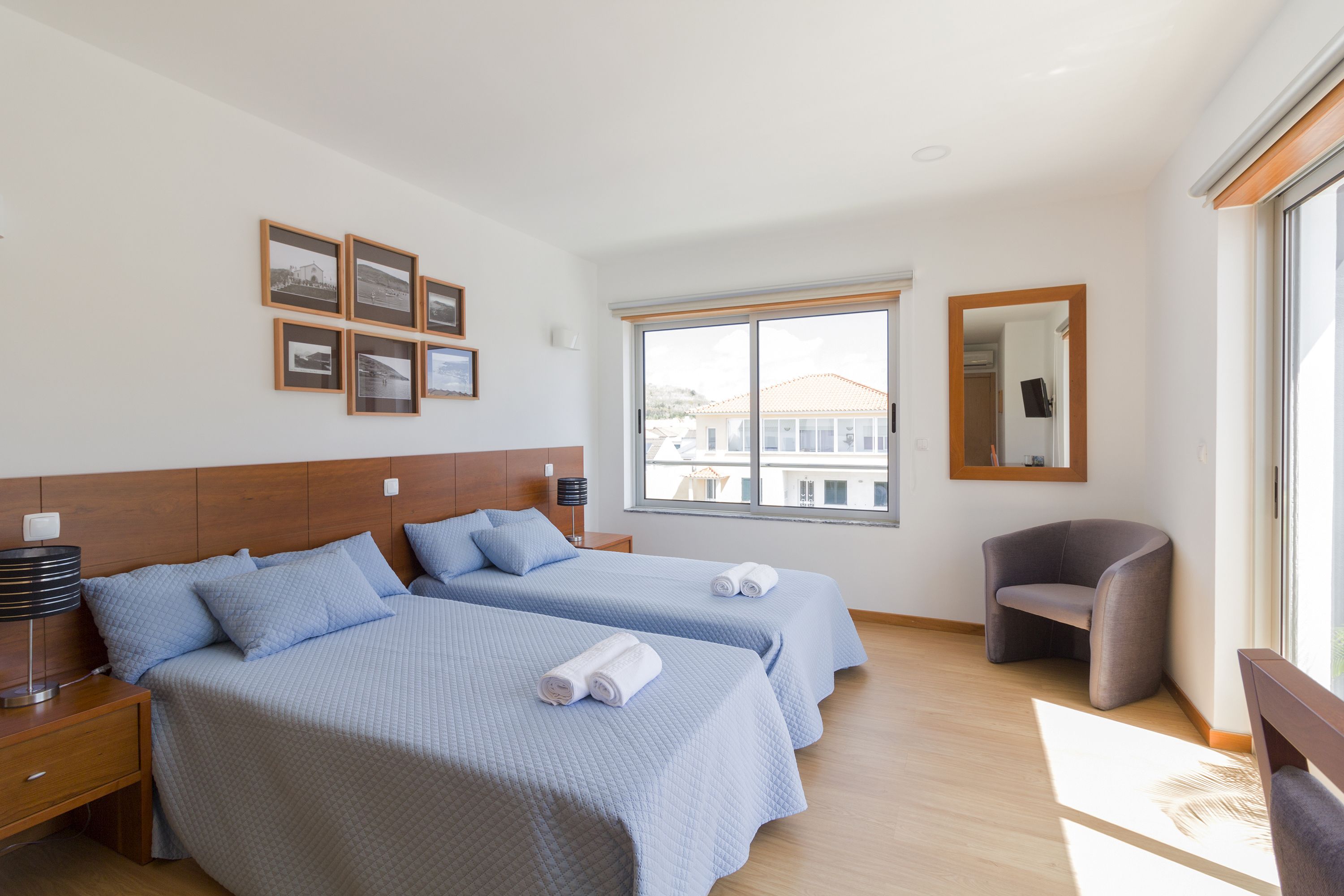 Ett hotellrum med två sängar, ett fönster med utsikt, en stol och inramade tavlor på väggen.