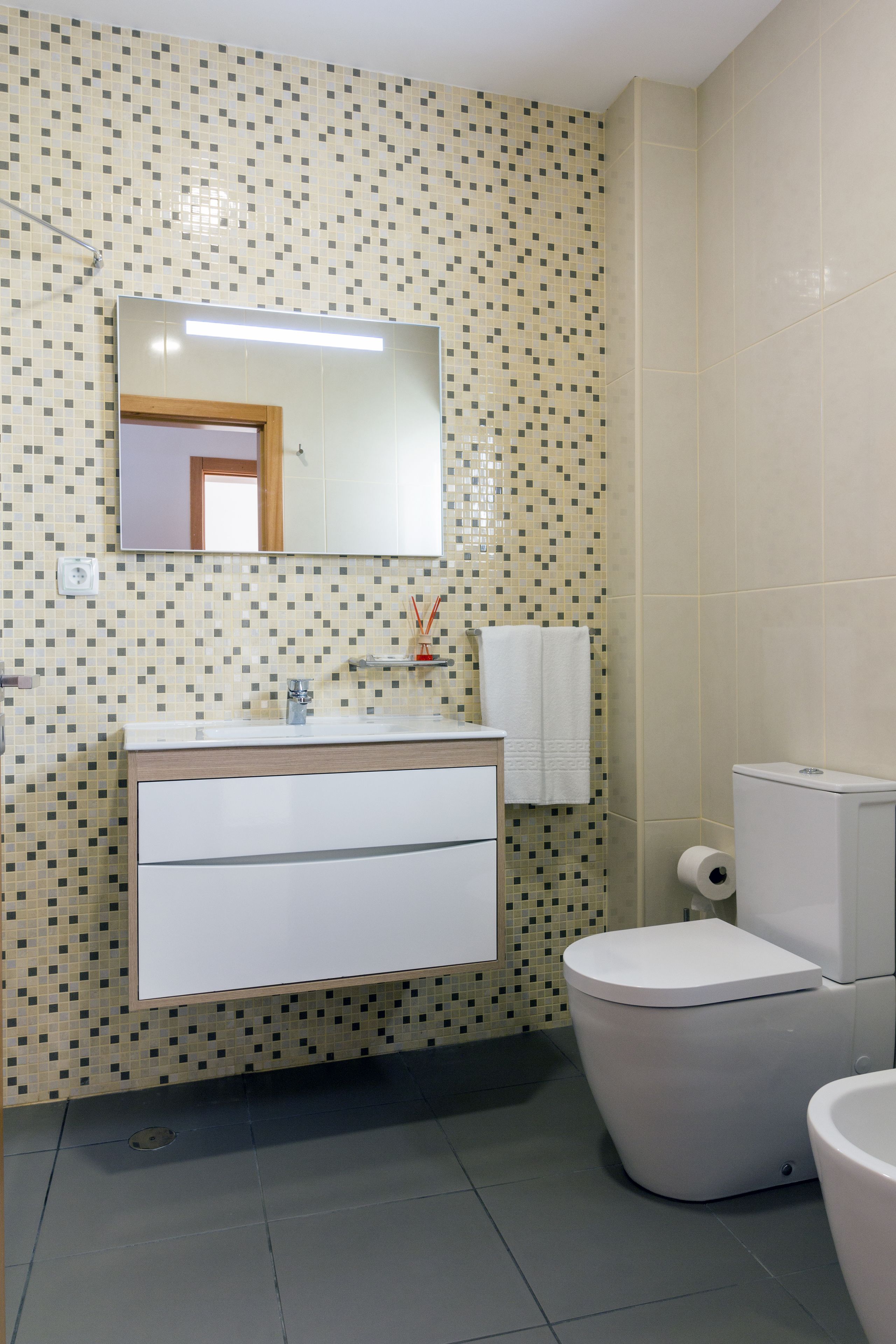 Une salle de bain avec un mur carrelé, un miroir, un lavabo, des toilettes et un porte-serviettes.