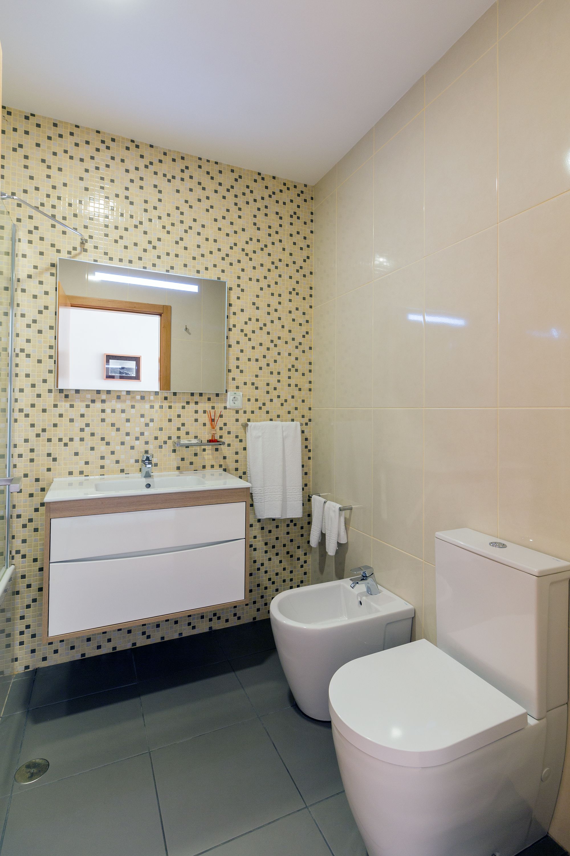 Une salle de bain avec un sol carrelé, un lavabo, un bidet, des toilettes et un miroir.
