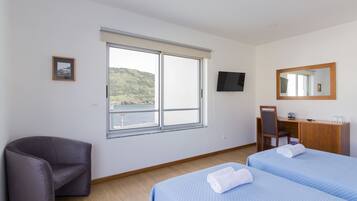 A hotel room with a large window, a desk, a chair, and two beds.
