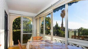 A sunroom with a large table and chairs, large windows, and a view of trees and buildings.