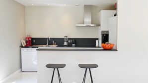 A modern kitchen with a dishwasher, a coffee machine, a blender, and a kettle on the counter. There are two black stools at the counter. - SEVRIER,Plain pied, Spacieuse Villa, jardin, 8pers (Sévrier)