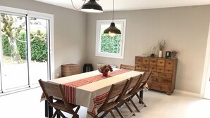 A dining area with a long table, wooden chairs, a wooden cabinet, and a window with a view of greenery. - SEVRIER,Plain pied, Spacieuse Villa, jardin, 8pers (Sévrier)