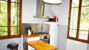 A compact kitchen with a wooden table, stools, a stove, and a window with a view of greenery. - ST-JORIOZ, maison de famille, 500m du Lac, 10M de la piste cyclable, 10pers (Saint-Jorioz)