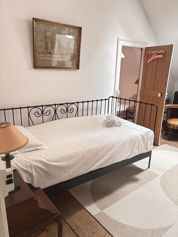 Een slaapkamer met een bed, een bureau, een lamp, een lijst met een afbeelding en een deur.