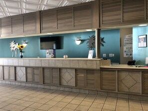 Un área de recepción con pared color turquesa, un televisor de pantalla plana y un mostrador con un jarrón de girasoles.