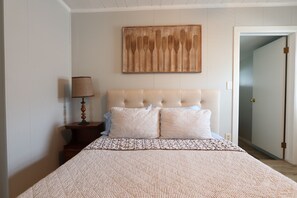 A bedroom with a bed, a nightstand, a lamp, and a wall-mounted artwork.
