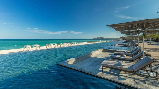 Un espace aménagé au bord de la piscine, avec des chaises longues et des parasols, donnant sur une plage.