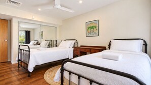 A hotel room with two single beds, a wooden desk, a mirror, and a framed picture on the wall.