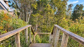 A wooden staircase leading to a forested area with a building in the background. - Penguins Rest – situated in the award-winning Tilbury Cove (Culburra Beach)