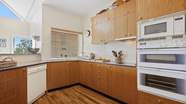 A kitchen with wooden cabinets, a Bosch microwave, and a Bosch oven. - Penguins Rest – situated in the award-winning Tilbury Cove (Culburra Beach)