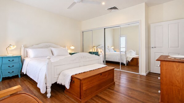 A bedroom with a bed, a bedside table, a mirror, a wooden bench, and a wardrobe. - Penguins Rest – situated in the award-winning Tilbury Cove (Culburra Beach)
