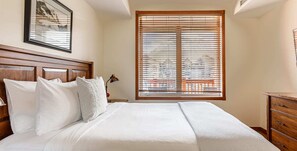 Relax in a spacious room with a large bed, framed artwork, and a window with horizontal blinds.