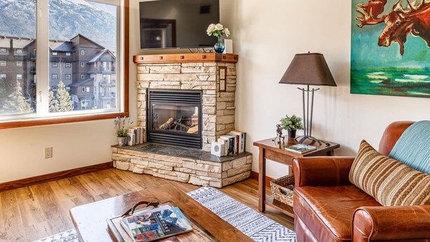 A living room with a stone fireplace, a sofa, a coffee table, and a painting on the wall. - Mountain Paradise"at Falcon Crest Lodge (Canmore)