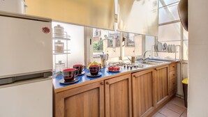 A kitchen with wooden cabinets, a white refrigerator, a sink, and a window with a view of buildings outside. - COLOSSEUM a stone's throw from (Roma)