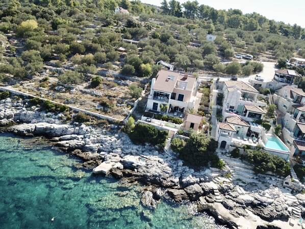 En ejendom ved kysten med et stort hus, en swimmingpool og klippeområde.