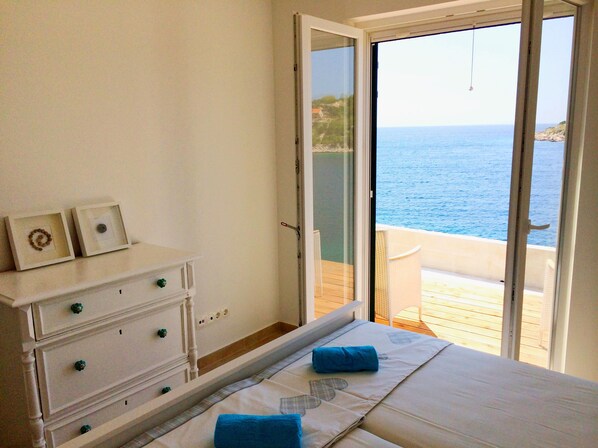 Un dormitorio con cama, cómoda y vista al mar por una puerta abierta.