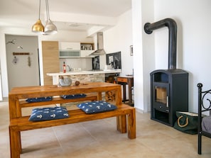 Una cocina moderna con una isla central, una mesa de comedor con bancos y una estufa de leña.