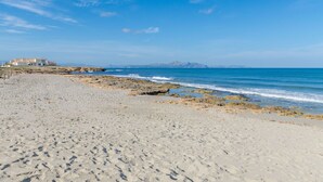 A beach with a rocky shoreline and a building in the background. - YourHouse Solmarina Son Serra (Son Serra de Marina)