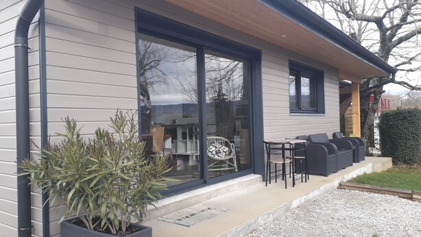 A modern house with a large sliding glass door, outdoor seating area, and a potted plant. - L'Ehappée Belle - 2 to 8 people - Lake view (Maisod)