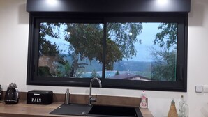 A kitchen with a black countertop, a sink, and a window with a view of trees and a distant landscape. - L'Ehappée Belle - 2 to 8 people - Lake view (Maisod)