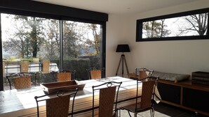 A modern dining area with a large table and chairs, a lamp, and a view of trees through large windows. - L'Ehappée Belle - 2 to 8 people - Lake view (Maisod)