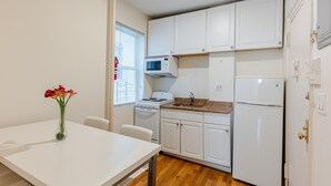 Cocina compacta con armarios blancos, microondas, estufa y refrigerador. Hay una mesa de comedor con un jarrón de flores.