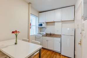 A compact kitchen with white cabinets, a microwave, stove, and refrigerator. There is a dining table with a vase of flowers.
