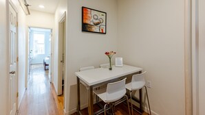 Un comedor con una mesa blanca, cuatro sillas y un florero con flores.