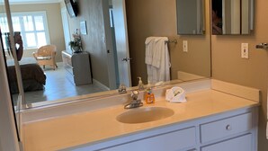 A bathroom with a large mirror, a sink with a soap dispenser, and a towel rack.