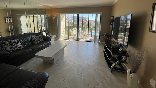 A modern living room with a black leather sofa, a white coffee table, and a flat-screen TV.