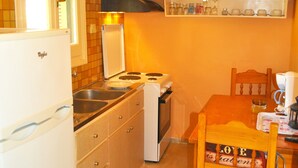 Een kleine keuken met een koelkast, fornuis, spoelbak en houten keukenkastjes.