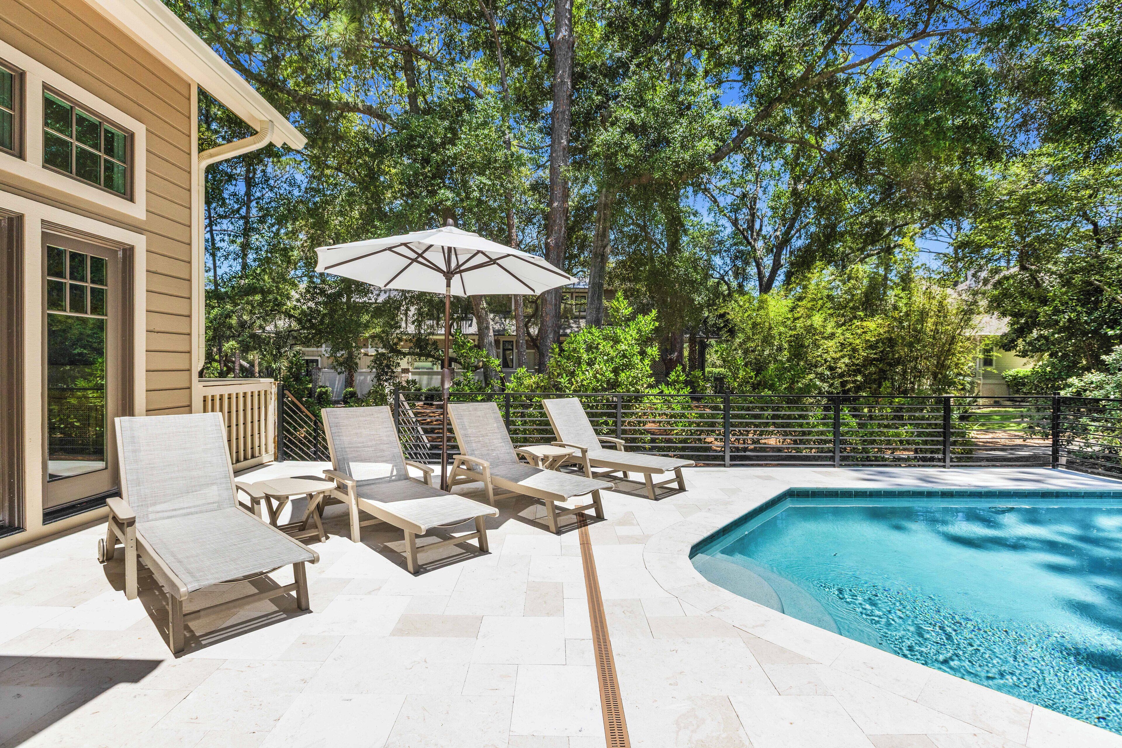 Un área junto a la piscina con sillones de descanso y una pérgola.