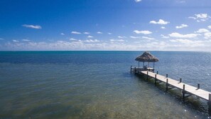 Une jetée s’avançant dans une mer calme, avec une structure à toit de chaume à son extrémité.