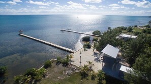 Vue aérienne d’une zone côtière avec une longue jetée s’étendant dans l’eau, un petit bâtiment et une végétation luxuriante.