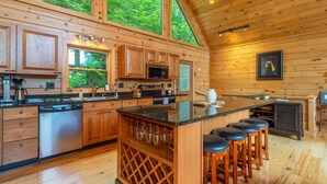 Una cocina moderna con armarios de madera, una isla central con taburetes y ventanas amplias con vistas al bosque.