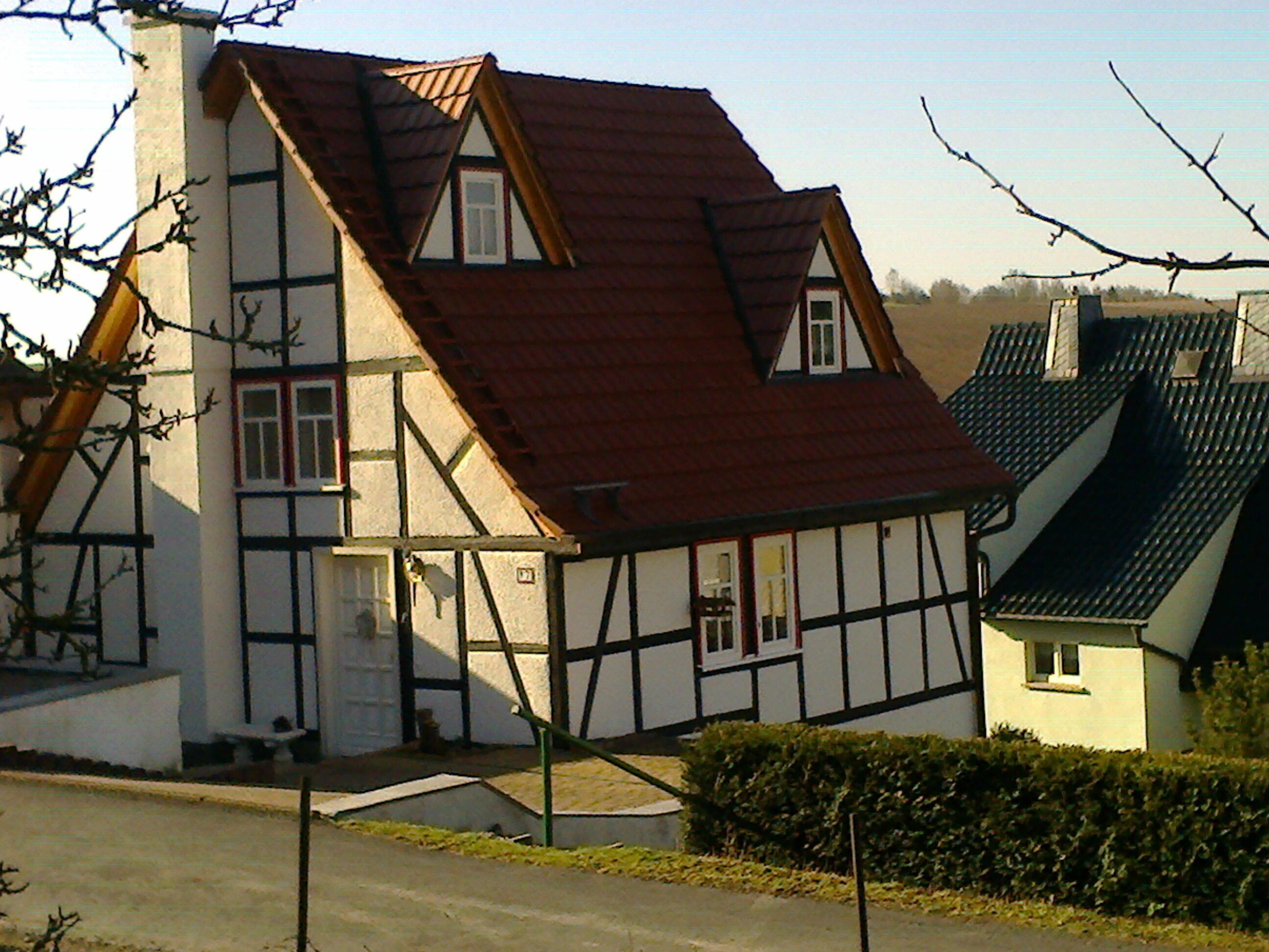 A traditional half-timbered house with a steeply pitched roof, a visible chimney, and a small front porch.