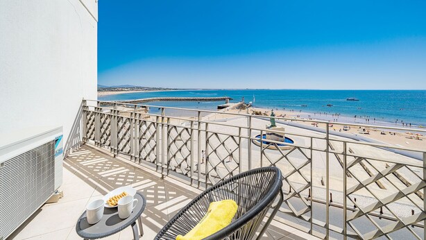 Un balcón con vista a la playa, una silla y una mesa con un plato de comida.