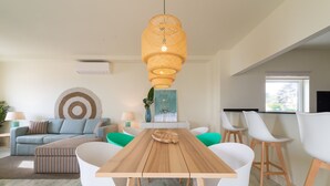 Una sala de estar moderna con una mesa de comedor de madera, sillas blancas, una lámpara colgante de ratán, un sofá y una mesa de centro.