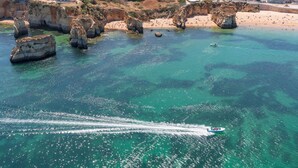 Un pueblo costero con una playa, formaciones rocosas y un barco en el agua.