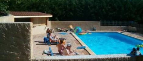 A swimming pool with a tiled deck, surrounded by a low wall and trees in the background.