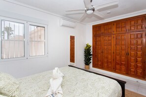 A bedroom with a bed, a ceiling fan, a potted plant, and a large wooden wardrobe.
