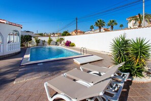 Una piscina con sillas de descanso y un pequeño jardín.
