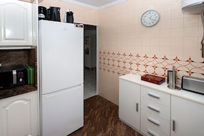 Une cuisine avec un réfrigérateur blanc, un four à micro-ondes et un grille-pain posés sur le plan de travail, une horloge au mur et des carreaux décoratifs sur le pare-feu.