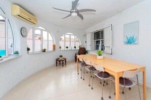 A spacious dining area with a long wooden table and chairs, a ceiling fan, and large windows with arched tops.