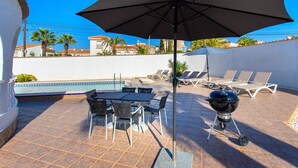 A patio with a pool, lounge chairs, a table, and a grill.