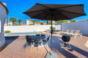 Un patio con piscina, sillas de descanso, una mesa y una parrilla.